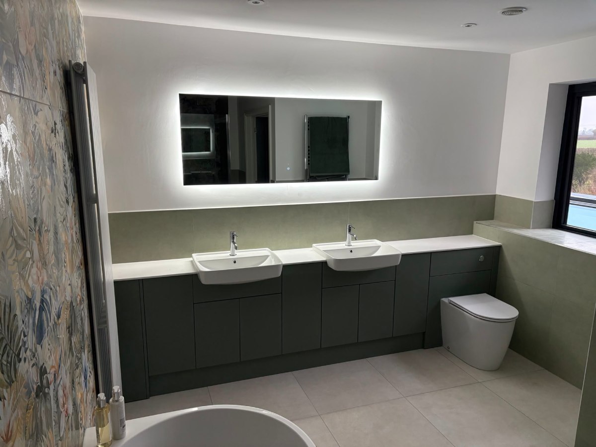 Double vanity bathroom with backlit mirror and sage green cabinetry